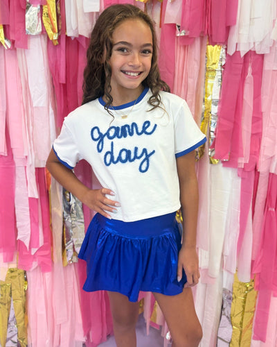 Young girl wearing a 'game day' shirt and blue skirt in front of a colorful background